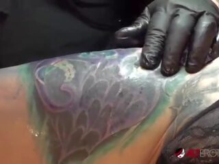 Marie Bossette touches herself while being tattooed